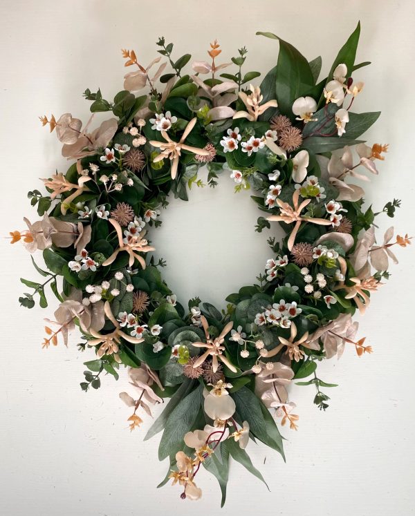 A circulation wreath filled with green eucalyptus leaves, pink kangaroo paw, white Geraldton wax flowers, baby’s breath and Billy buttons with longer gum leaves spiking out from the top and bottom of the wreath.