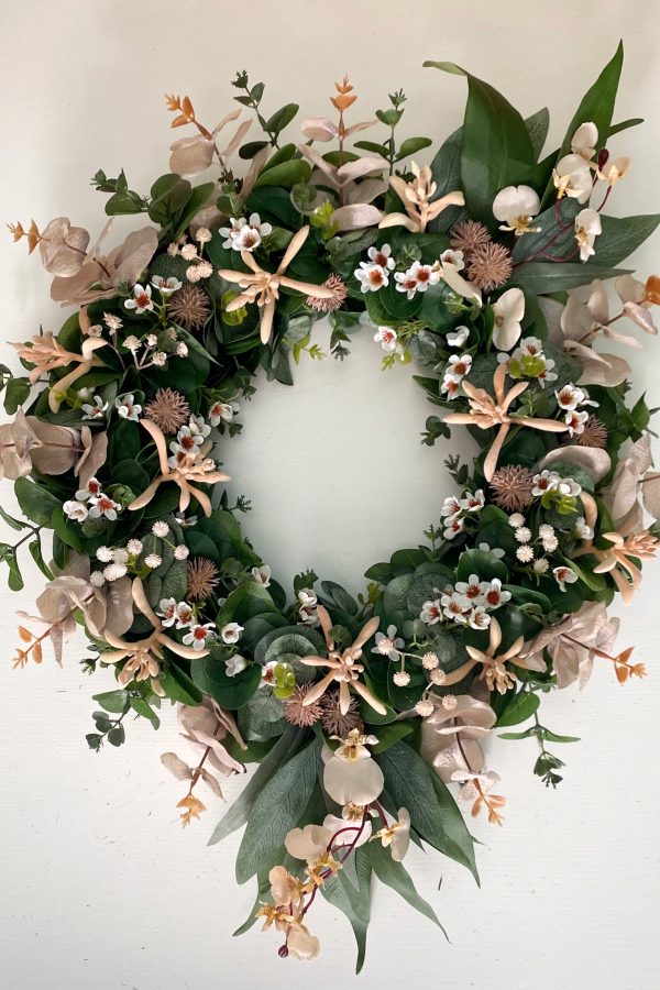 A circulation wreath filled with green eucalyptus leaves, pink kangaroo paw, white Geraldton wax flowers, baby’s breath and Billy buttons with longer gum leaves spiking out from the top and bottom of the wreath.