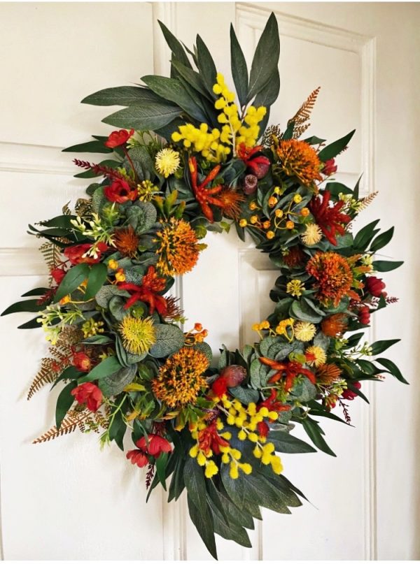 Native Christmas door wreath featuring artificial orange pincushion flowers, red berries, yellow billy buttons and long gum leaves protruding from the top and bottom with long sprigs of yellow wattle