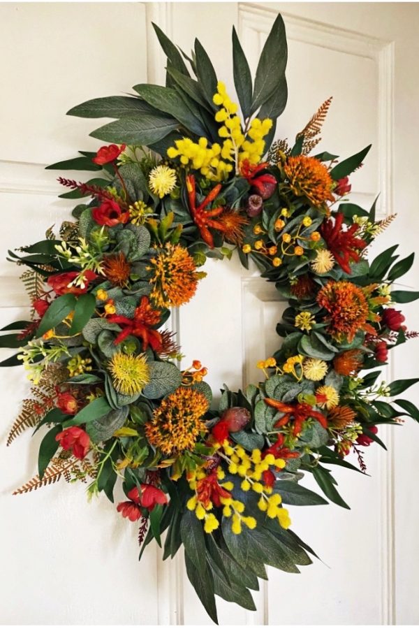 Native Christmas door wreath featuring artificial orange pincushion flowers, red berries, yellow billy buttons and long gum leaves protruding from the top and bottom with long sprigs of yellow wattle