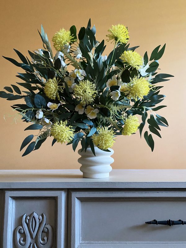 A vase of yellow pom Pom flowers set amongst eucalyptus leaves with some white gum blossoms