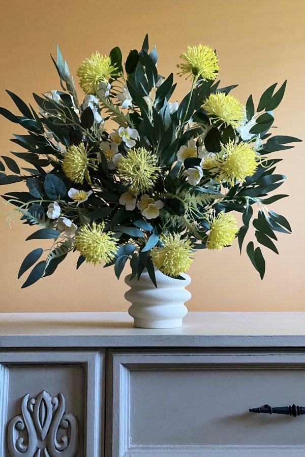 A vase of yellow pom Pom flowers set amongst eucalyptus leaves with some white gum blossoms